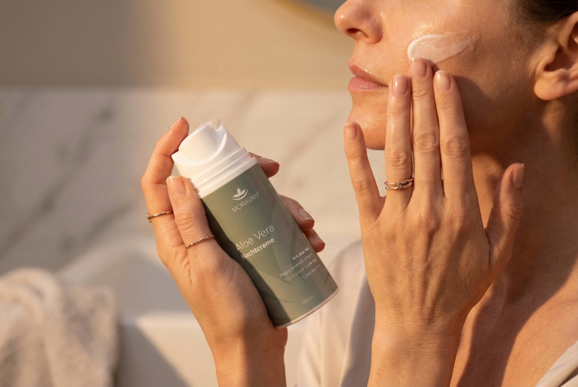 Close-up einer Hand die Nachtcreme aufträgt, warmes Abendlicht, Badezimmer-Atmosphäre